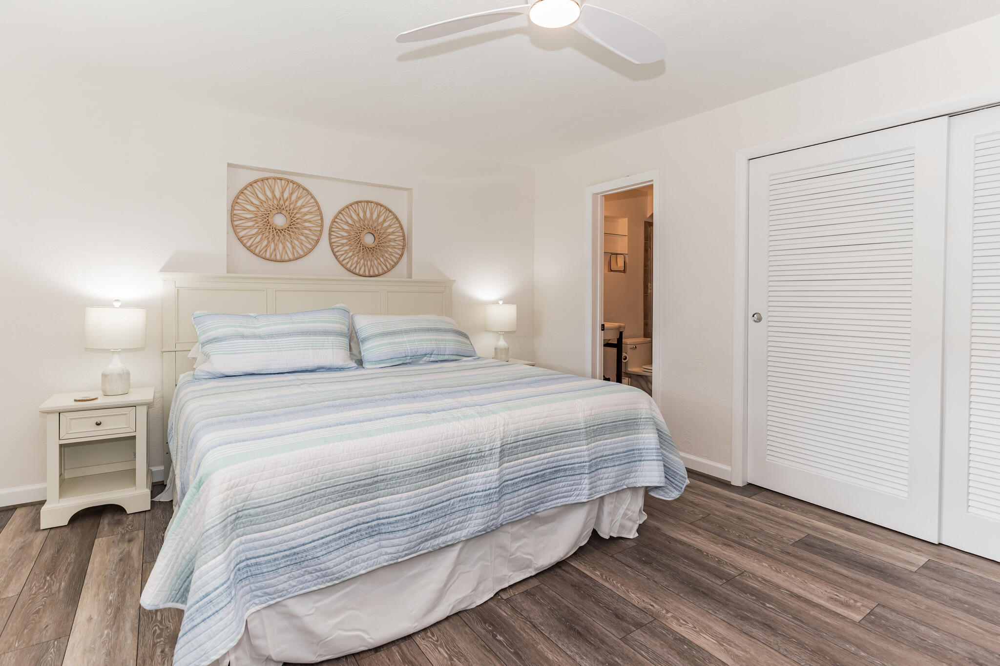 Furnished bedroom with striped bedding, woven wall decor, and an open doorway to an adjoining bathroom.