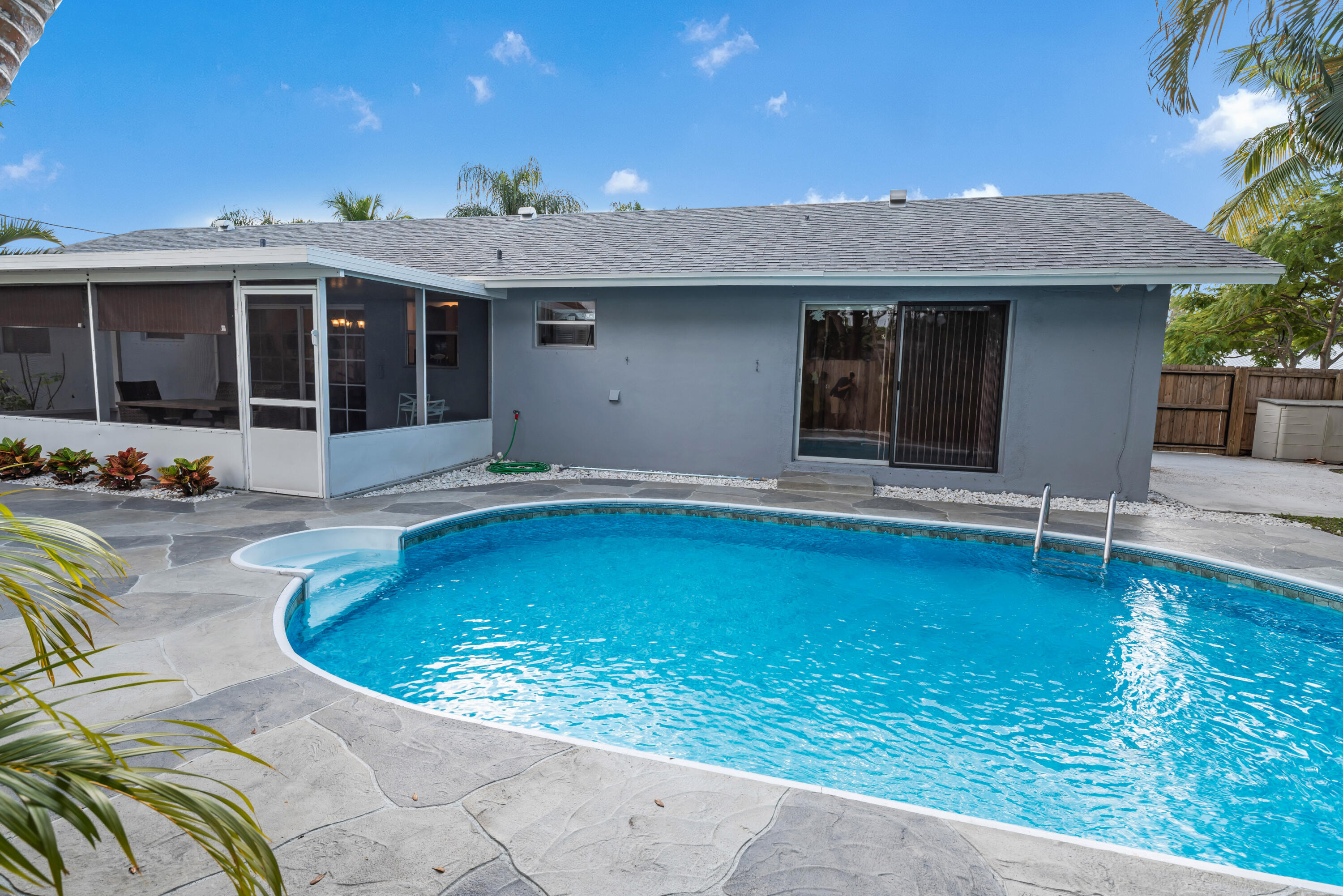 Back of a single-story home with a curved pool, stone patio, and screened porch.