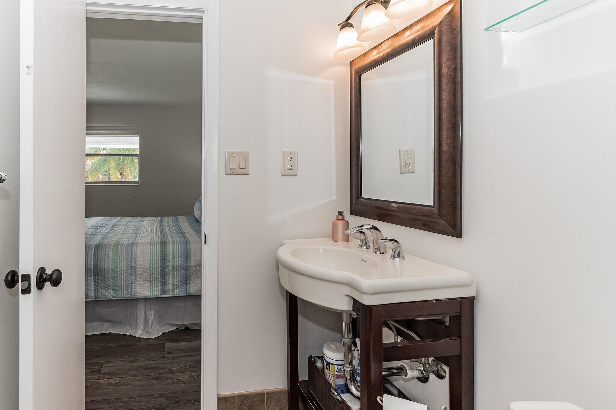Bathroom vanity with a white sink and dark wood cabinet beside an open doorway to a bedroom.