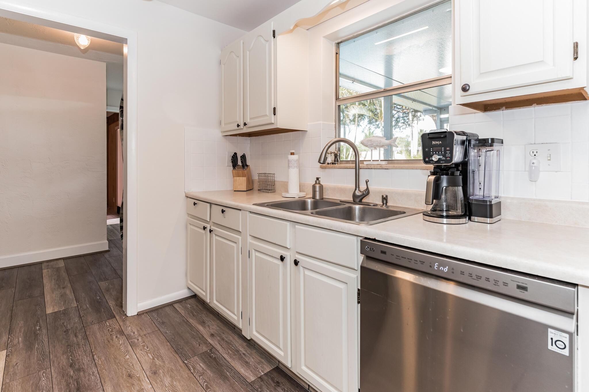 Kitchen with white cabinetry, a stainless double-basin sink, and a window overlooking palm trees.