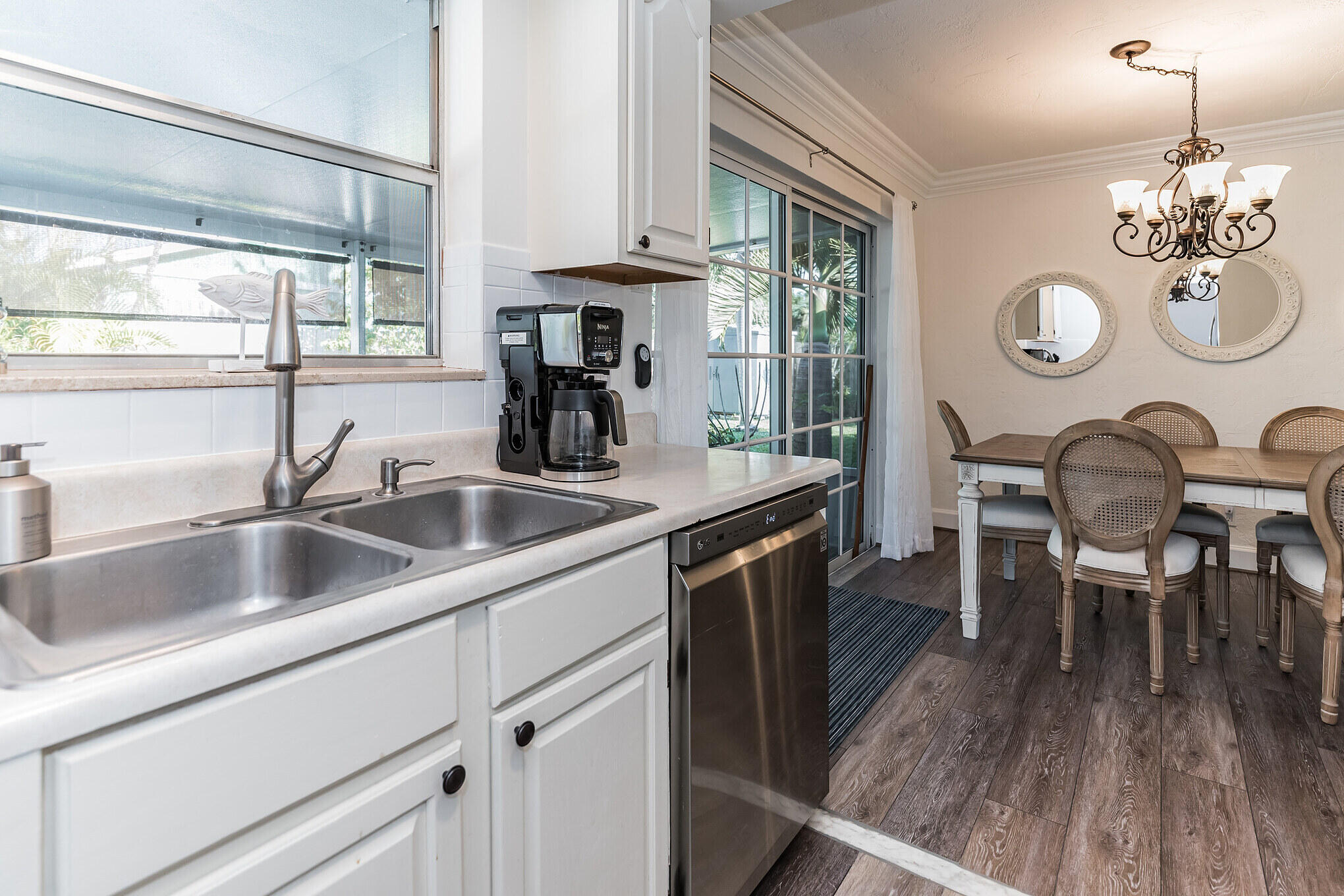 Kitchen and dining area with a double sink, stainless dishwasher, and dining table beside glass doors.