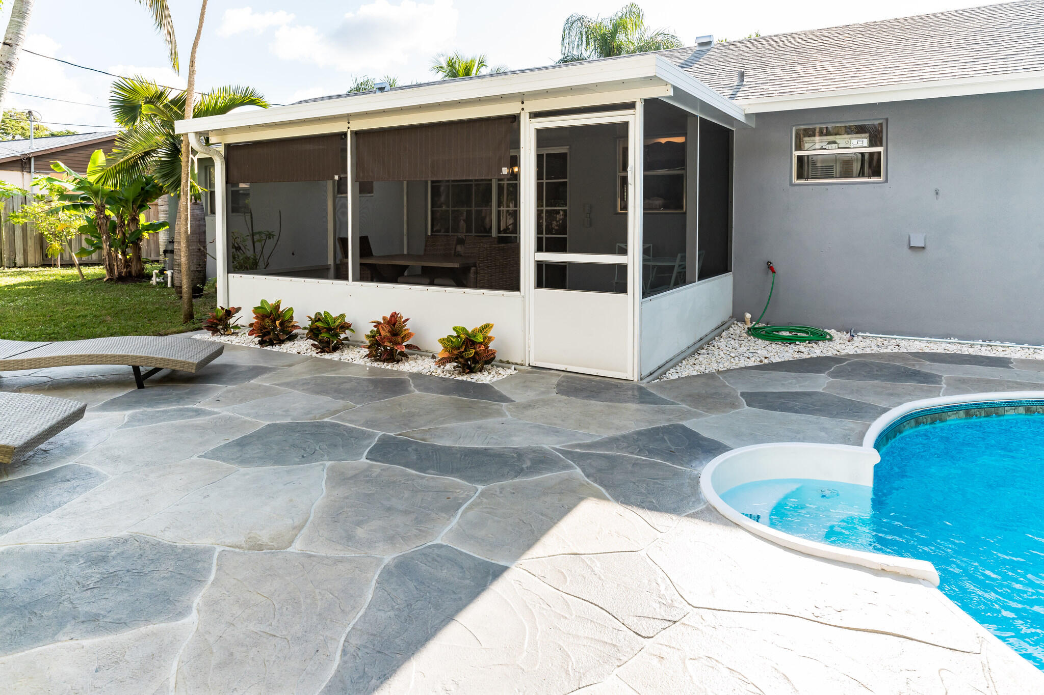 Backyard pool beside a screened patio, with a flagstone deck and tropical landscaping.