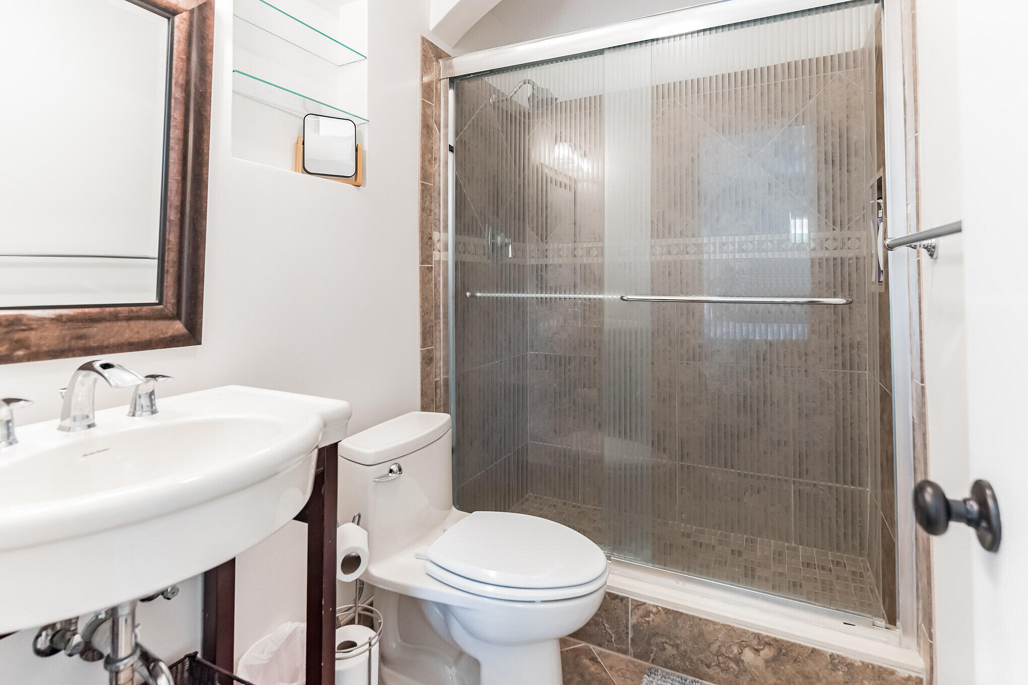 Bathroom with a pedestal sink, toilet, and glass-enclosed dark-tile shower.