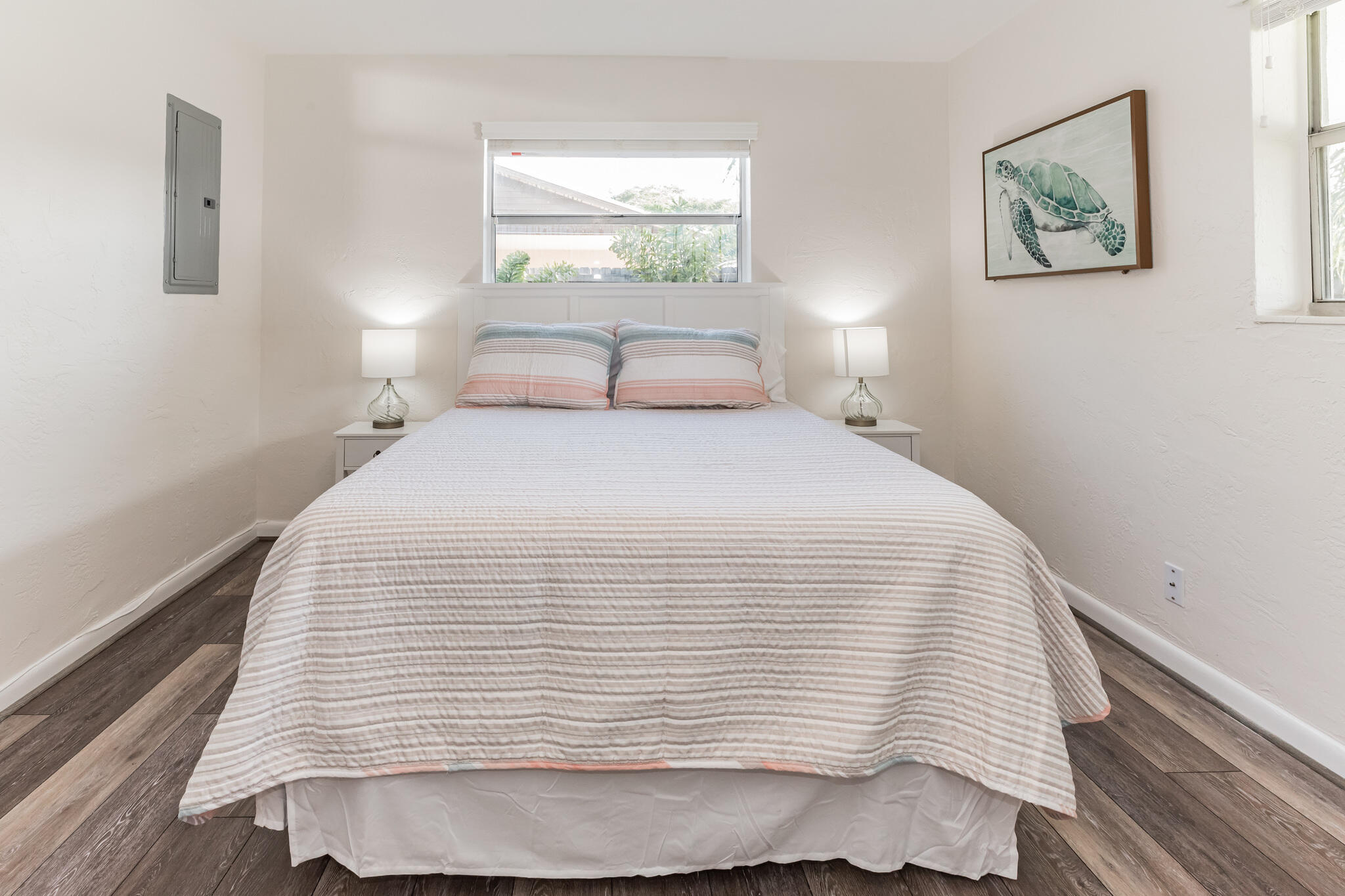 Staged bedroom with a striped bedspread, matching bedside lamps, and framed sea turtle artwork.