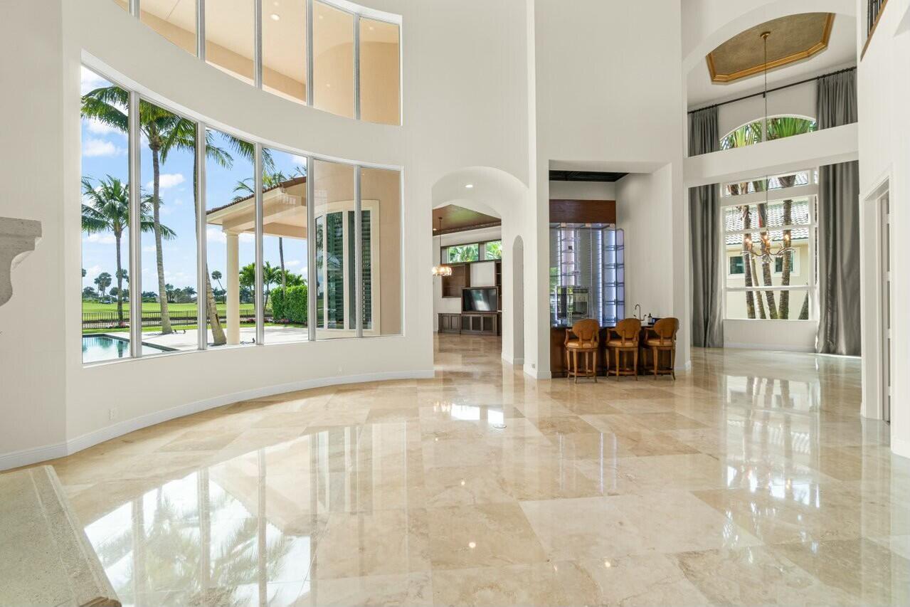 Double-height living area with glossy stone floors and windows overlooking palms, a pool, and a golf course.