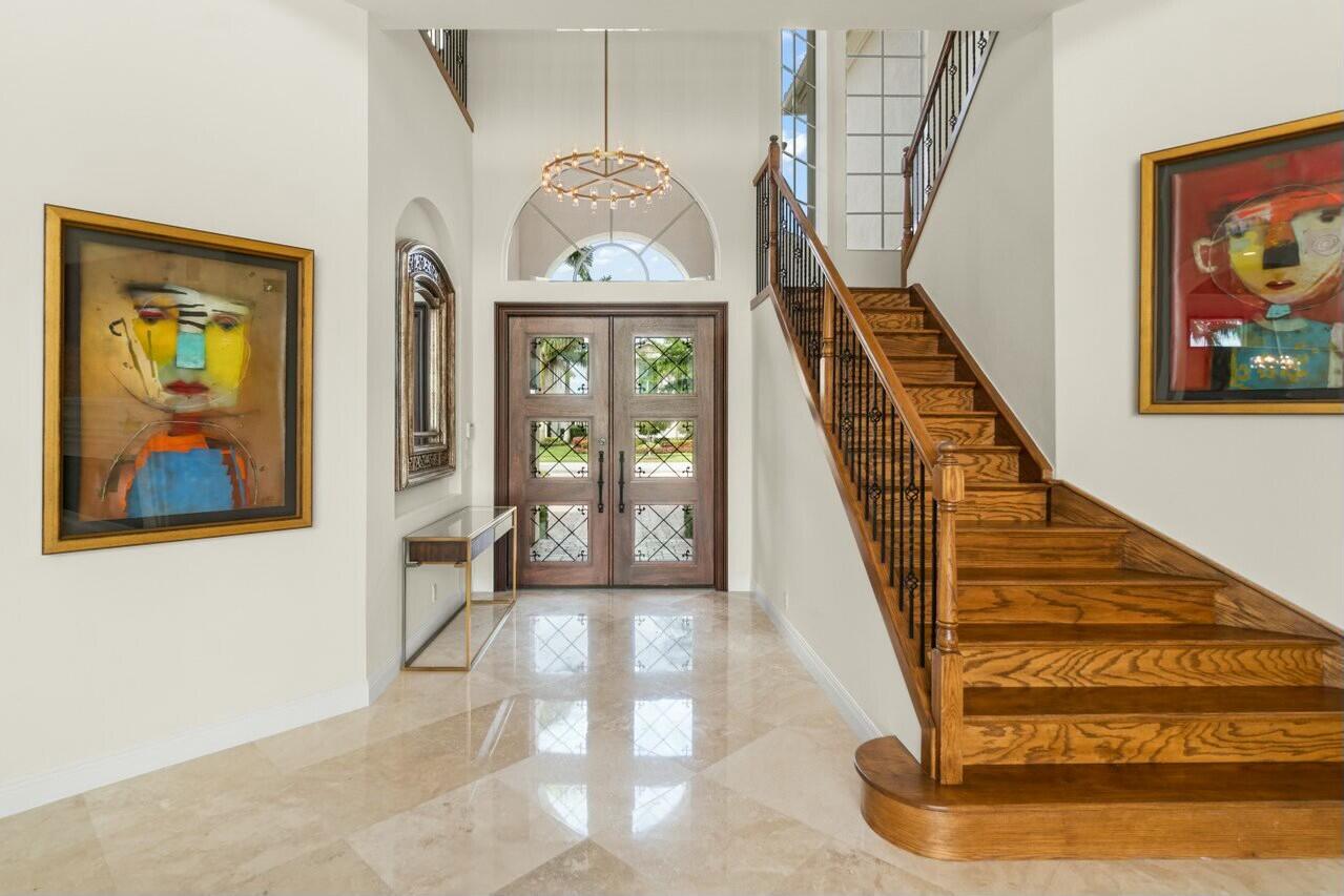 Two-story foyer with a wood staircase, marble floor, and glass-paneled double entry doors.