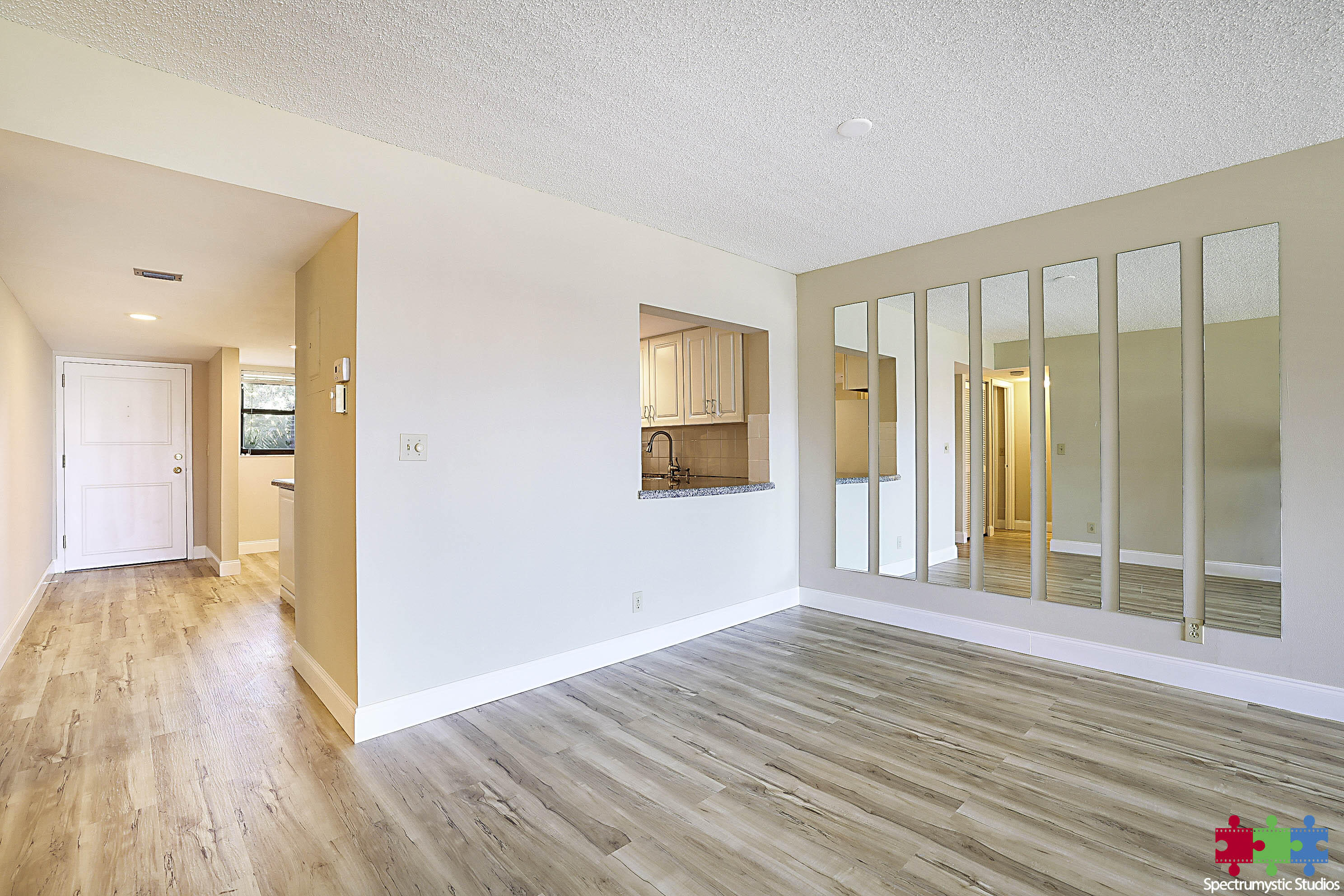 Vacant condo living area with wood-look floors, mirrored wall, and kitchen pass-through.