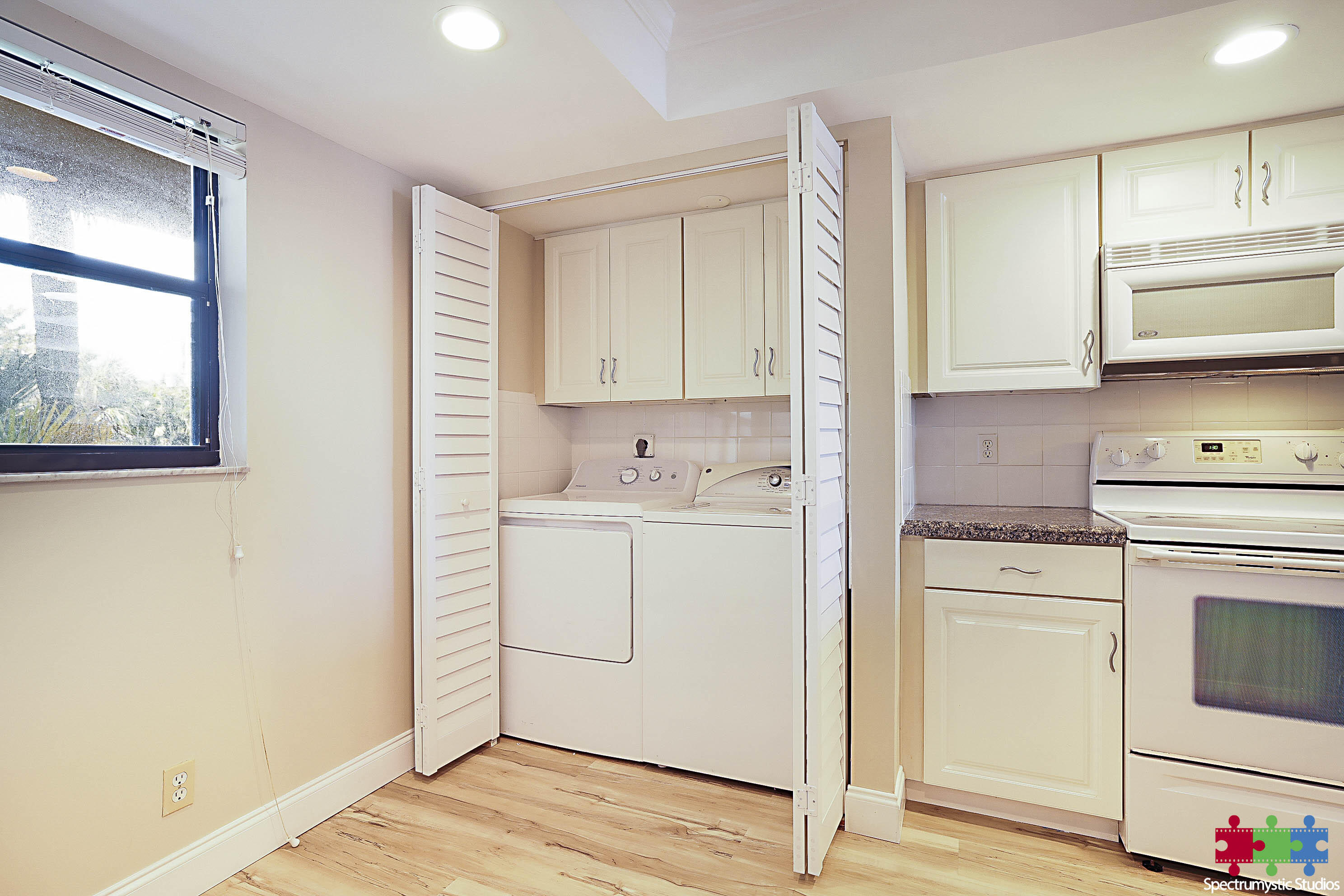 Kitchen with white cabinets and electric range beside an open laundry closet with washer and dryer.