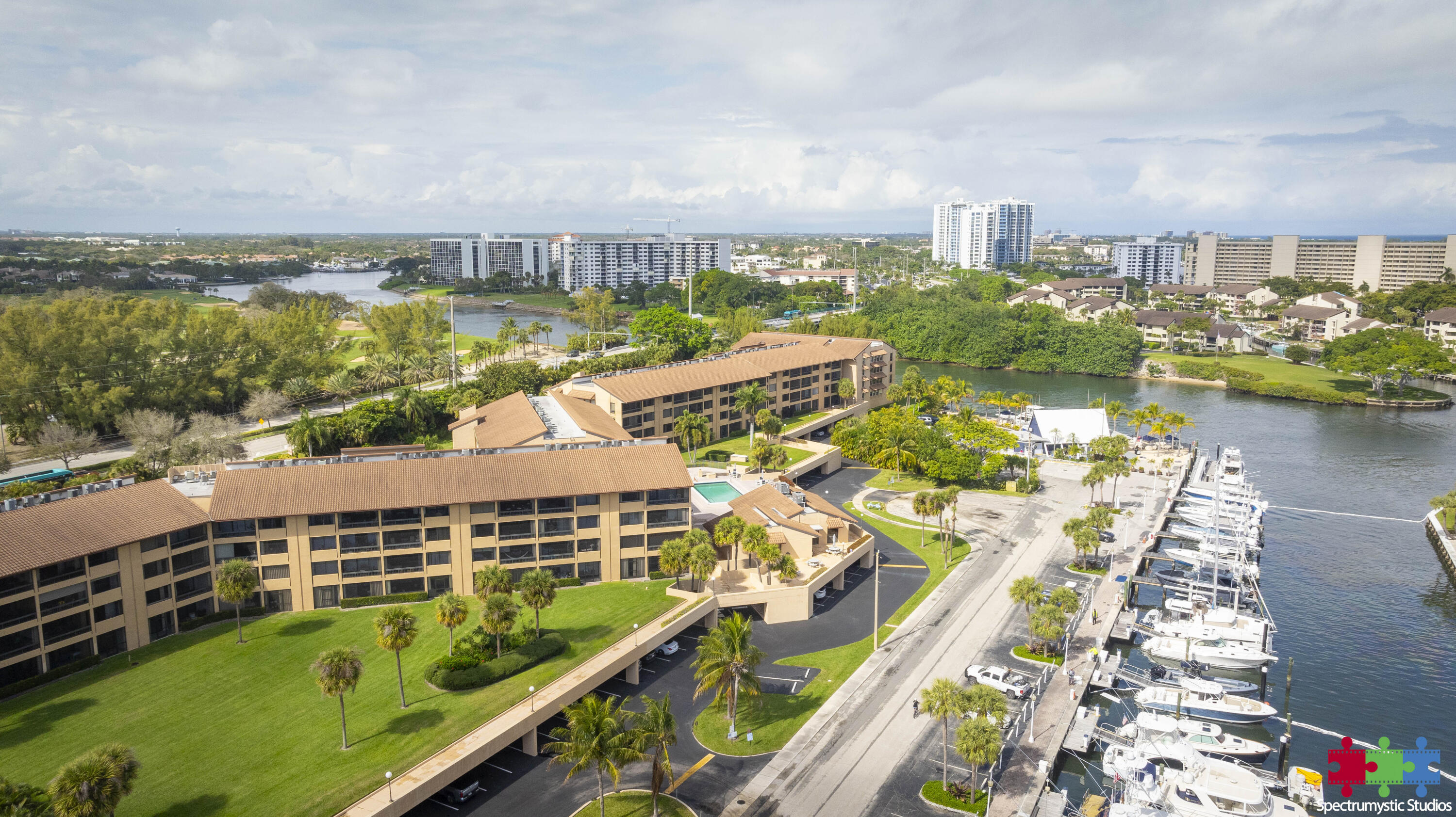 Waterfront condominium complex beside a marina, with boats, palm trees, and distant high-rises.