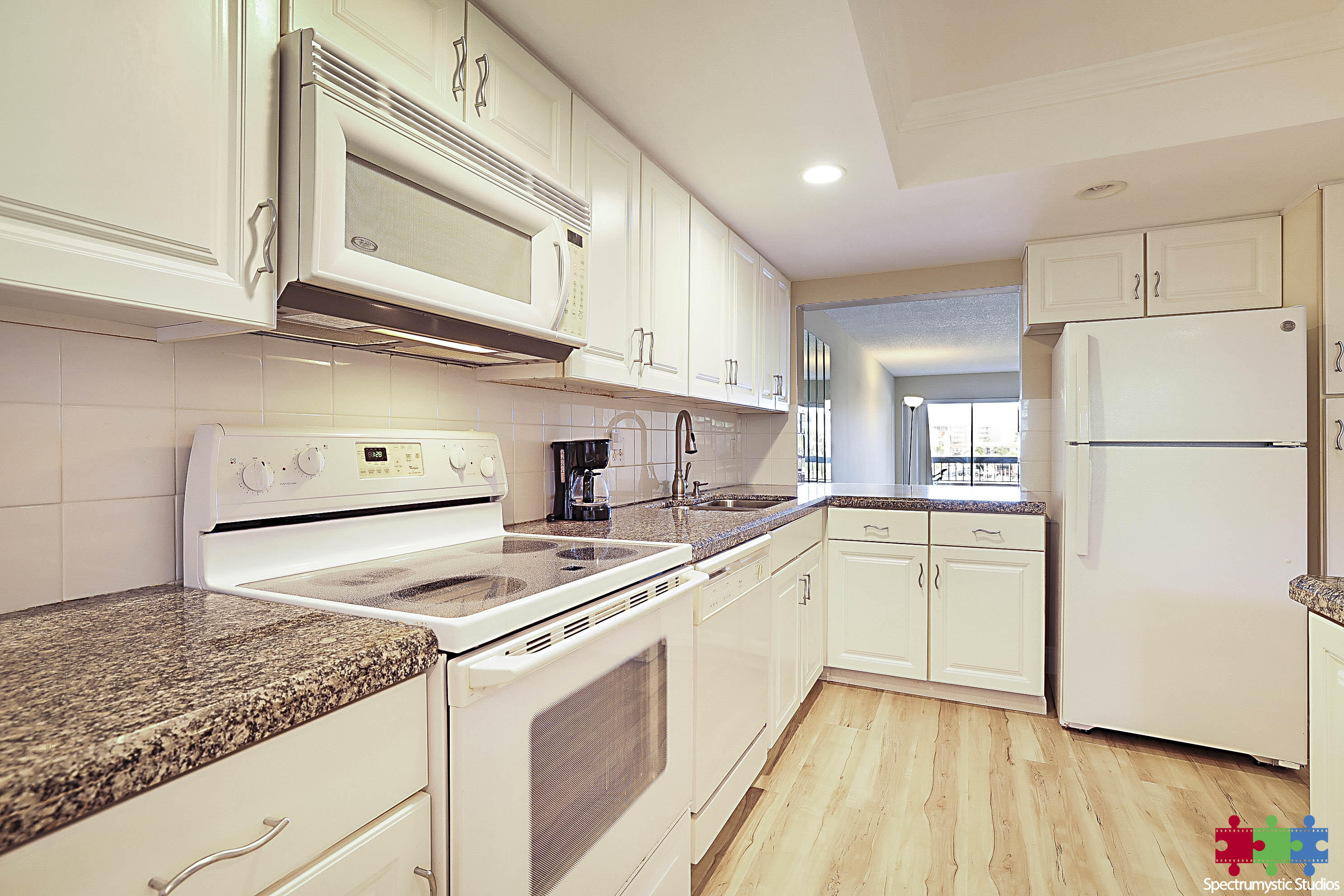 Condominium kitchen with white cabinets, granite counters, and a view toward the balcony.