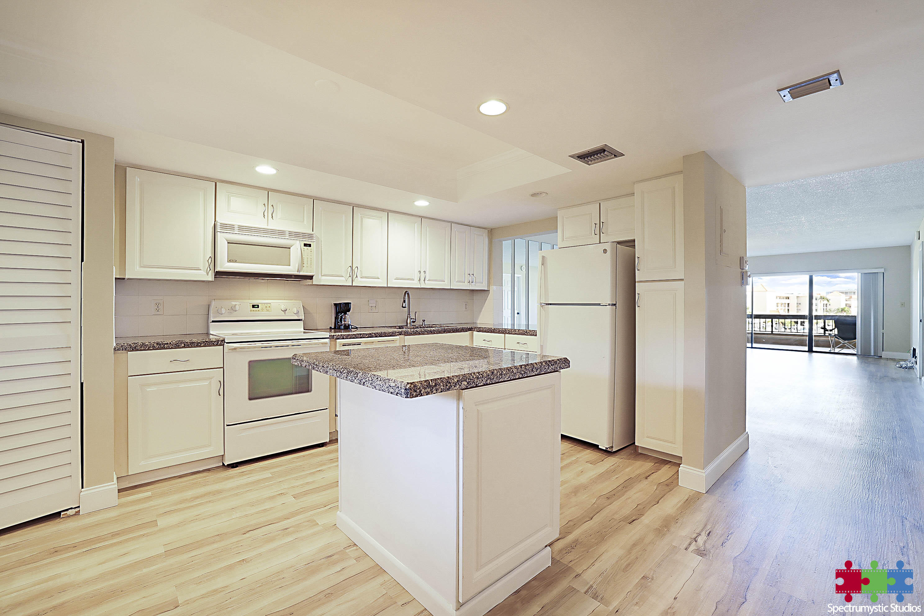 Condo kitchen with a granite-topped island, white cabinets, and an open view toward the balcony.