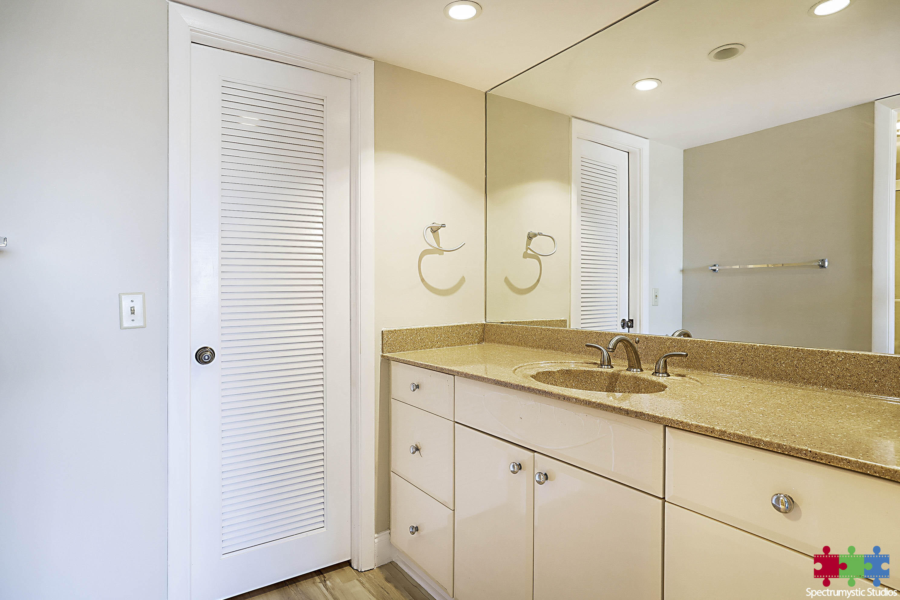 Bathroom vanity with a speckled countertop, single sink, large mirror, and white louvered door.