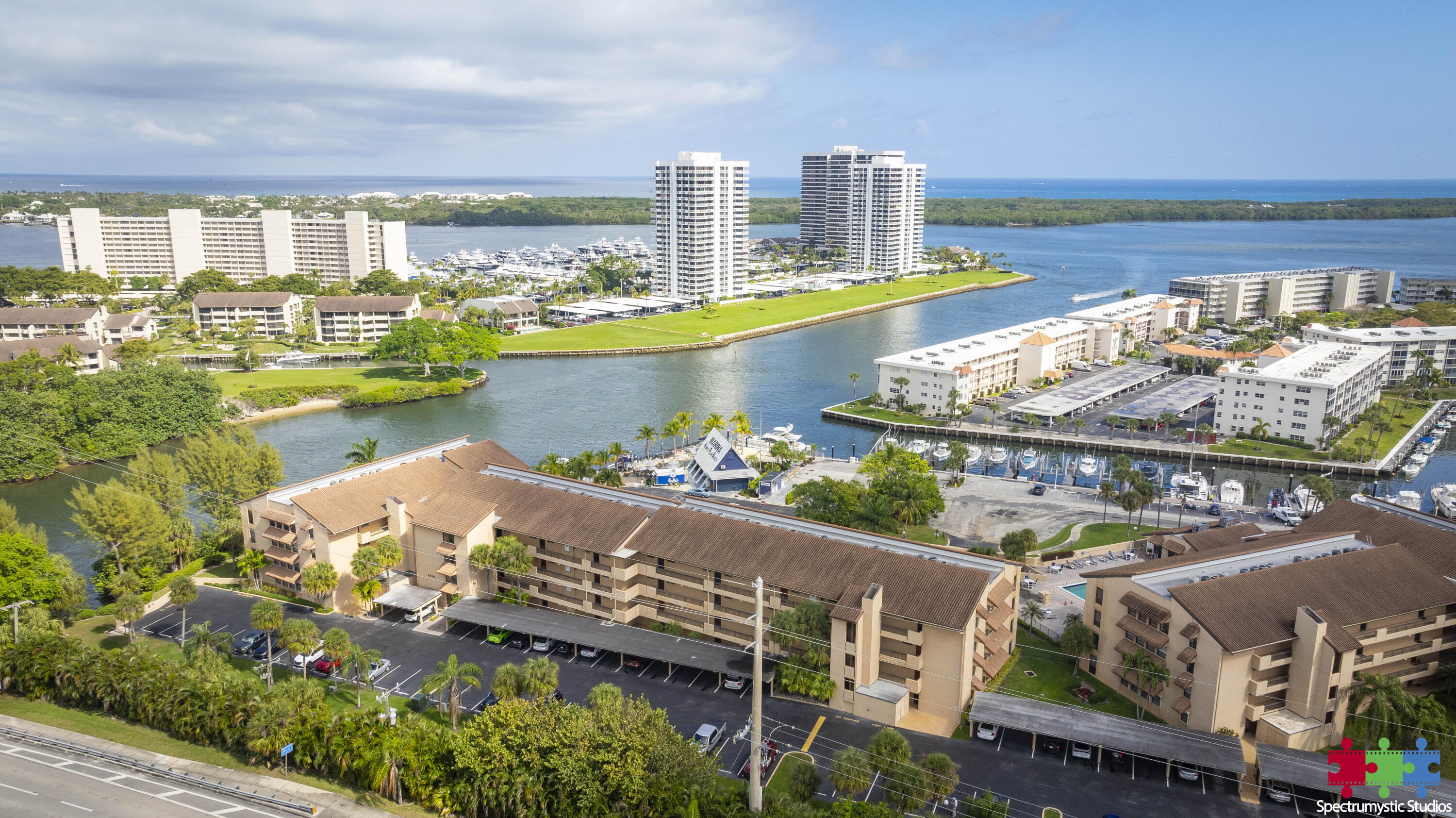 Waterfront condominium complex beside a marina, with boats and the ocean visible beyond the inlet.