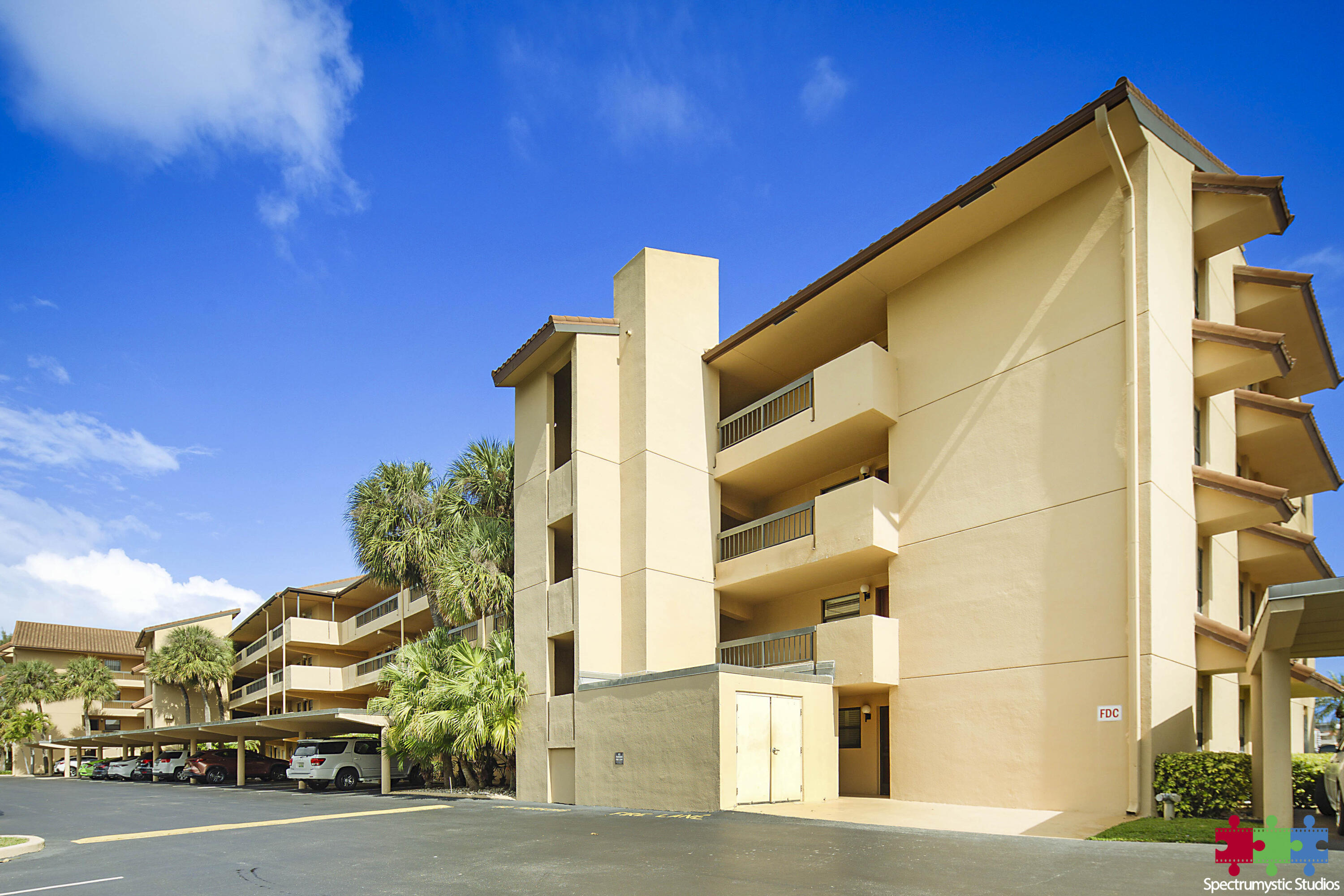 Condominium building with stacked balconies, palm trees, and covered parking.