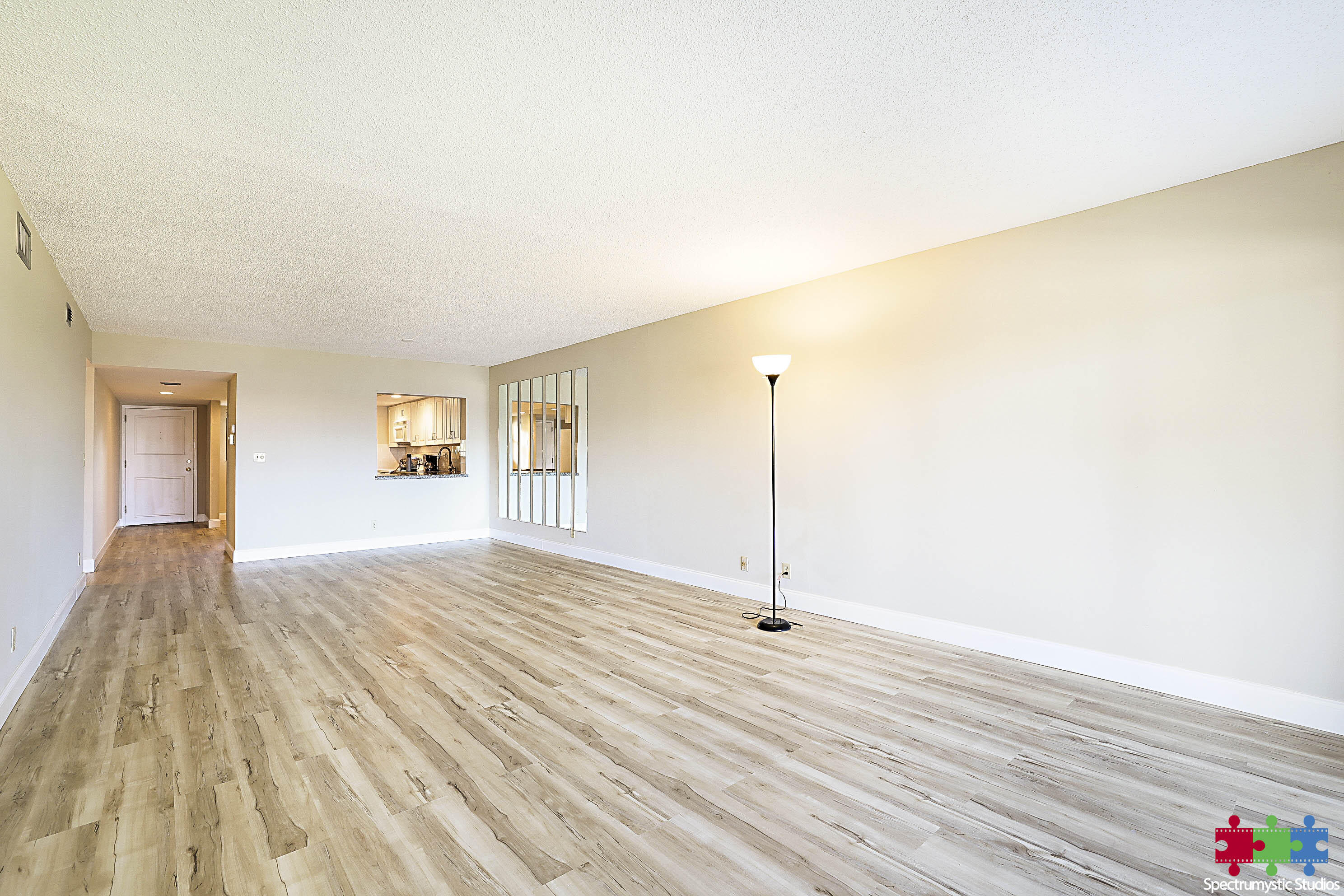 Empty living room with wood-look flooring, kitchen pass-through, and mirrored wall panels.