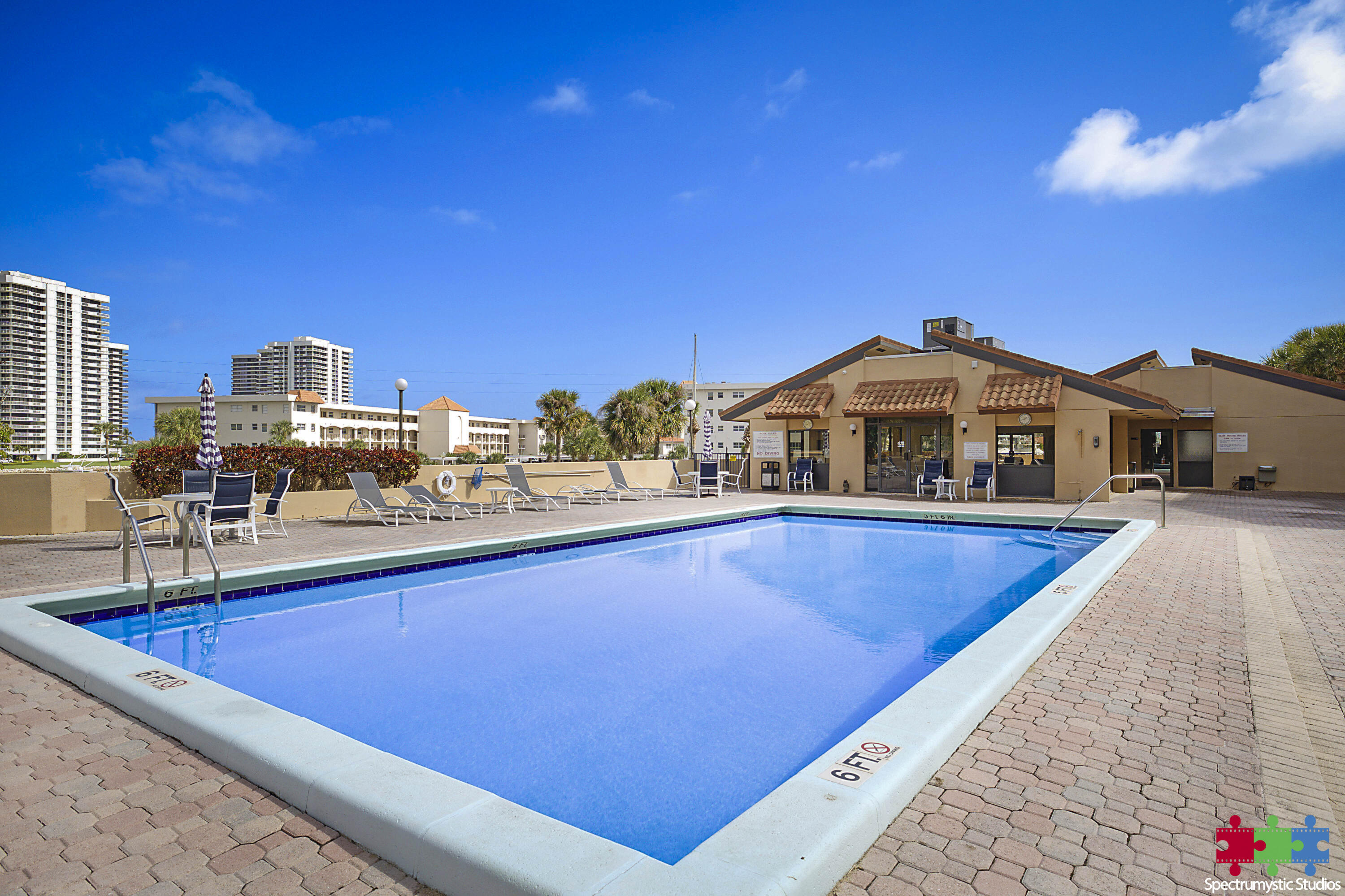 Outdoor pool with a paved deck, lounge chairs, and a cabana building.