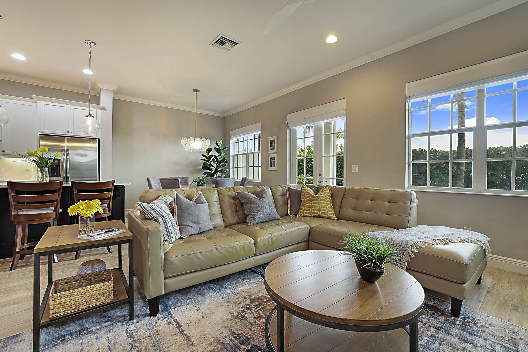 Furnished living room with a tan sectional, round coffee table, and large windows beside the dining area.