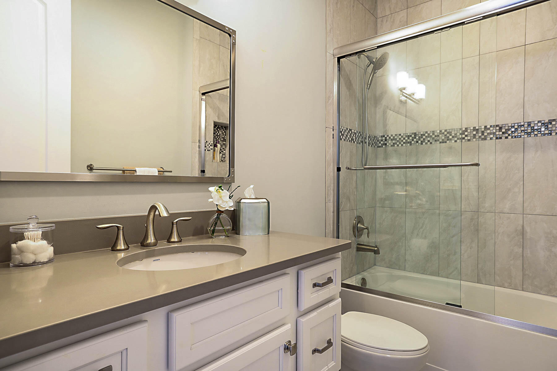 Bathroom with a pale vanity and glass shower featuring tiled walls and a mosaic accent strip.