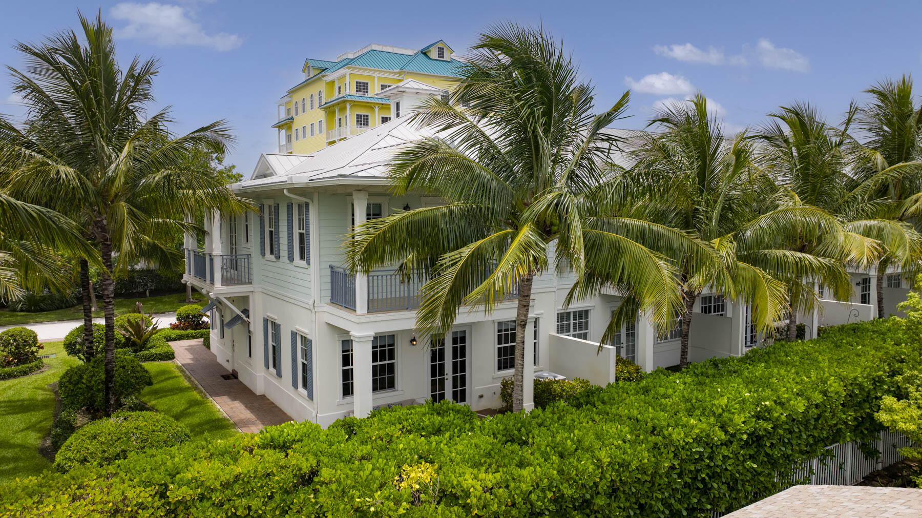 White coastal home with balconies, framed by palms, with a yellow tower rising behind it.