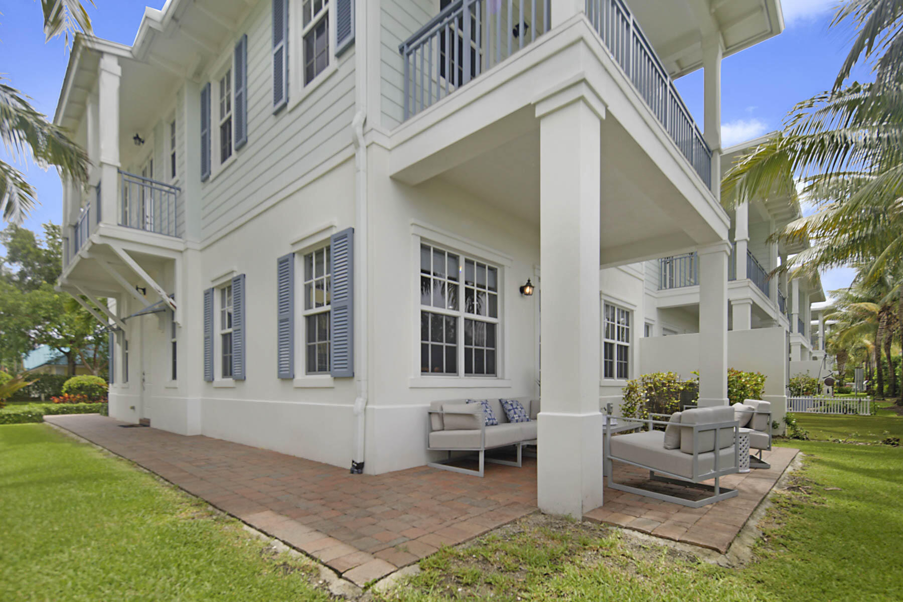 White coastal-style home with upper balconies and a covered patio furnished with outdoor seating.