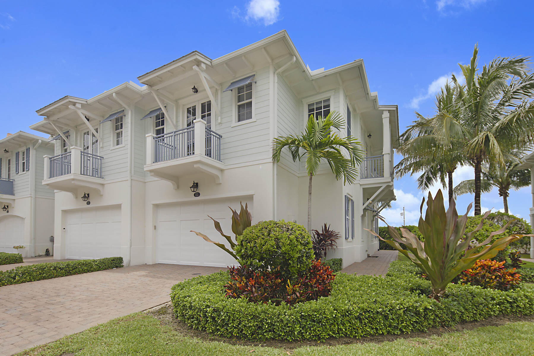 White two-story coastal home with balconies, garage doors, and tropical landscaping.
