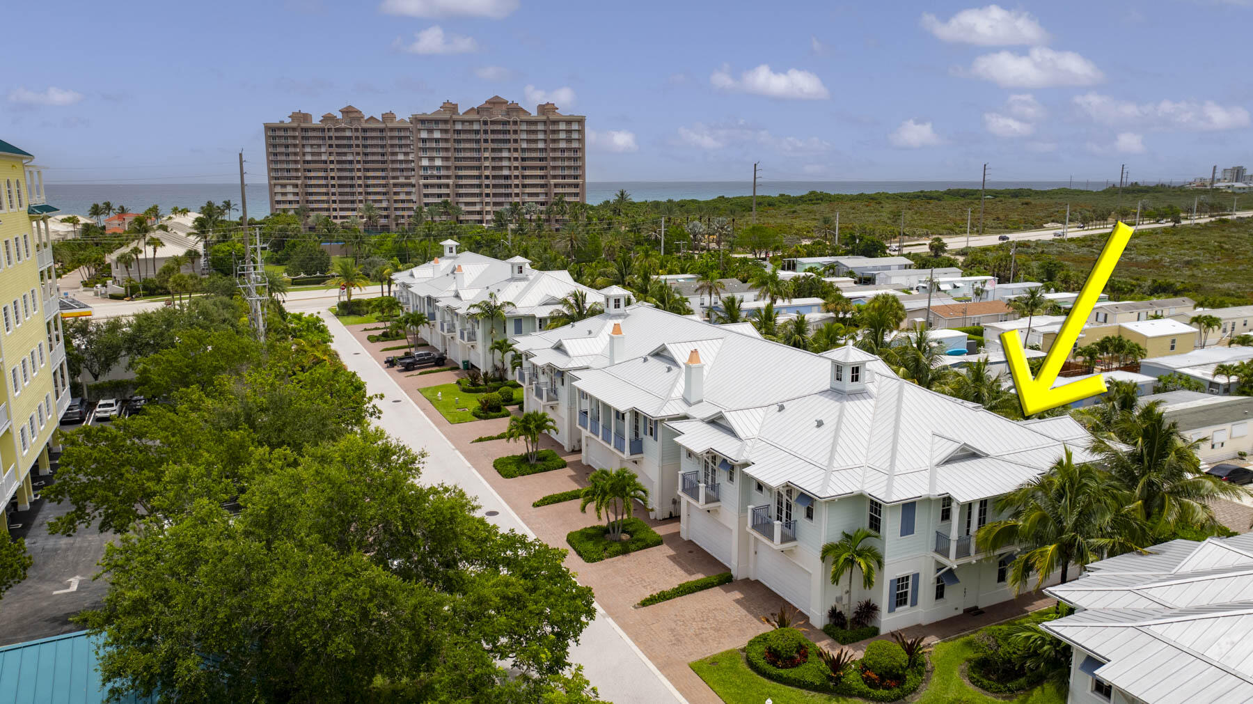 Aerial view of coastal homes near the ocean, with a yellow arrow pointing to one residence.