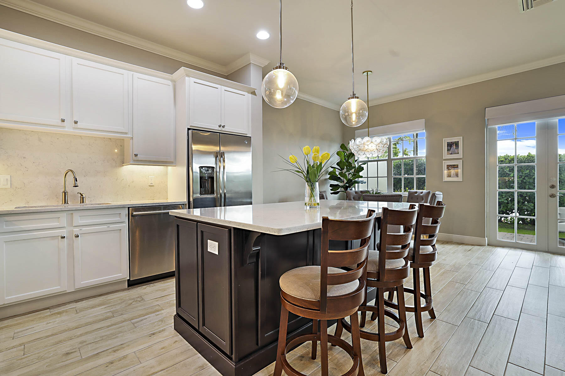 Kitchen with a dark island, wooden bar stools, white cabinets, and stainless steel appliances.
