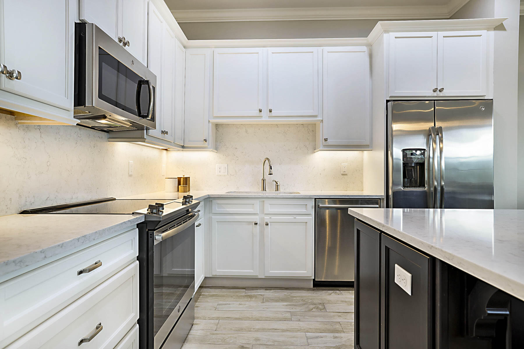 Kitchen with white cabinetry, stainless steel appliances, and a dark island with a marble-look countertop.