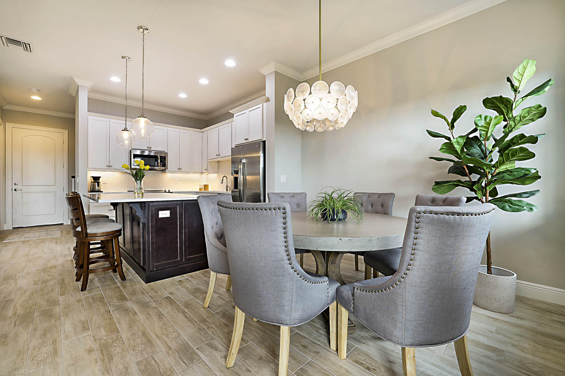 Open-plan kitchen and dining area with a dark island, stainless appliances, and a round table beneath a chandelier.