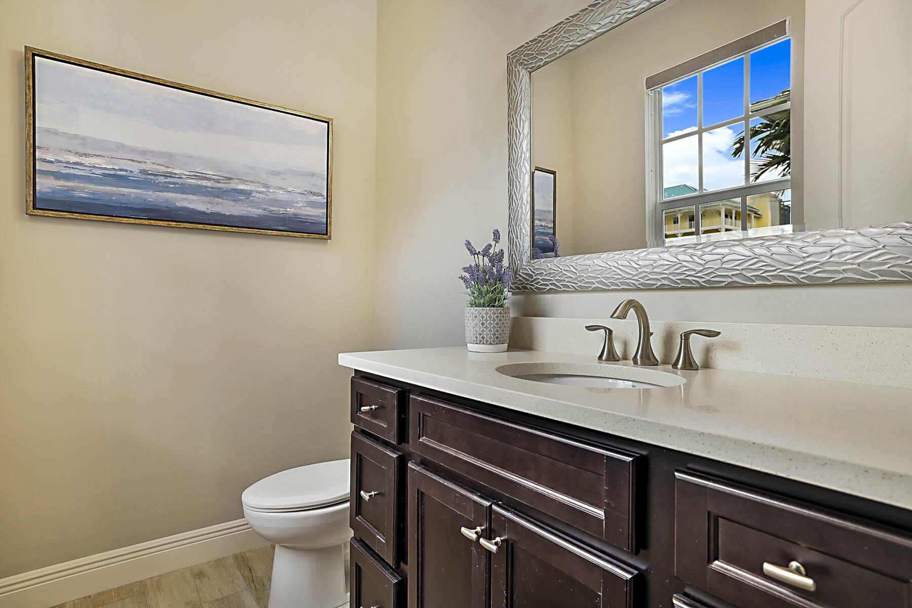 Bathroom with dark wood vanity, white sink, large mirror, and a window.