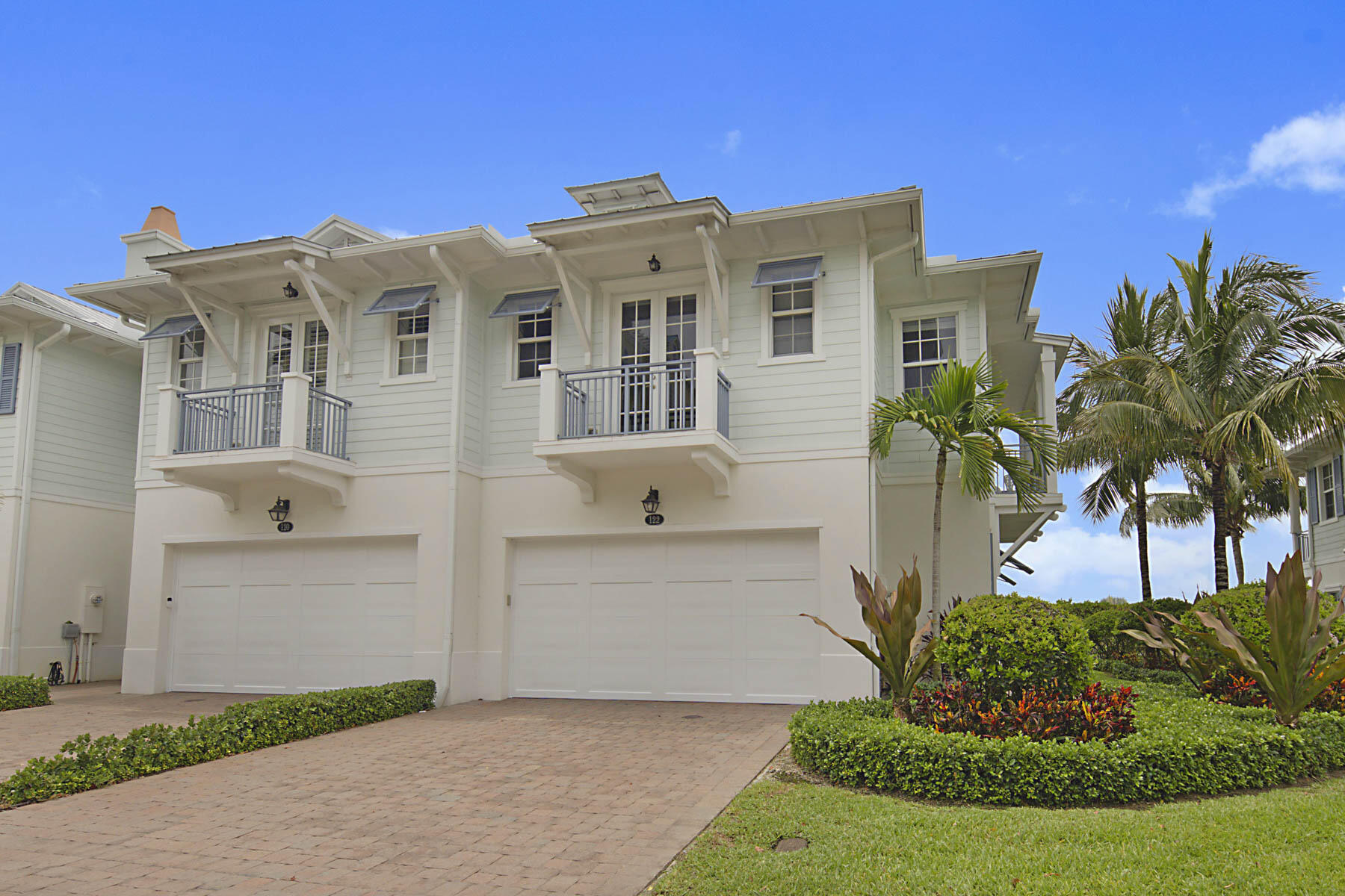 White coastal-style home with two garage doors, upper balconies, and palm landscaping.