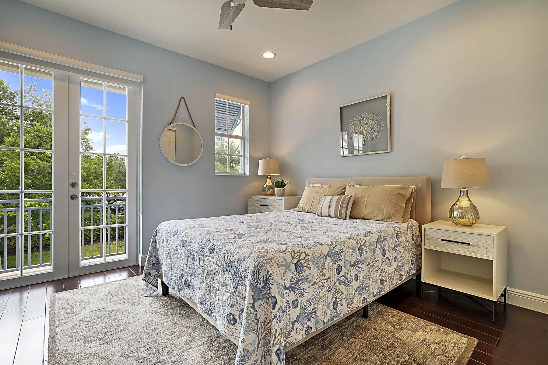 Staged bedroom with a patterned king bed and glass doors opening onto a leafy balcony.