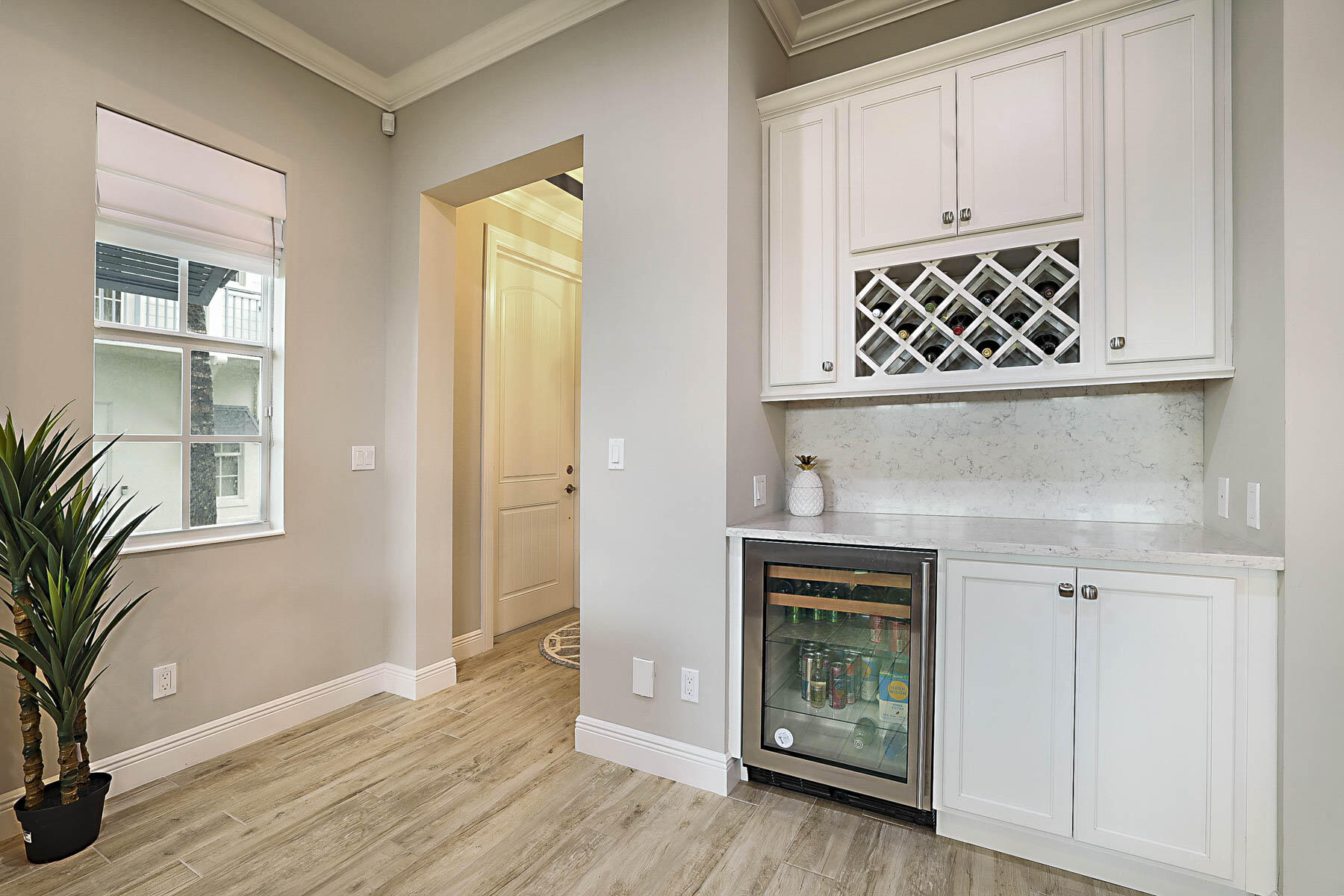 Built-in wine bar with white cabinets, diamond wine rack, stone backsplash, and glass-front beverage refrigerator.