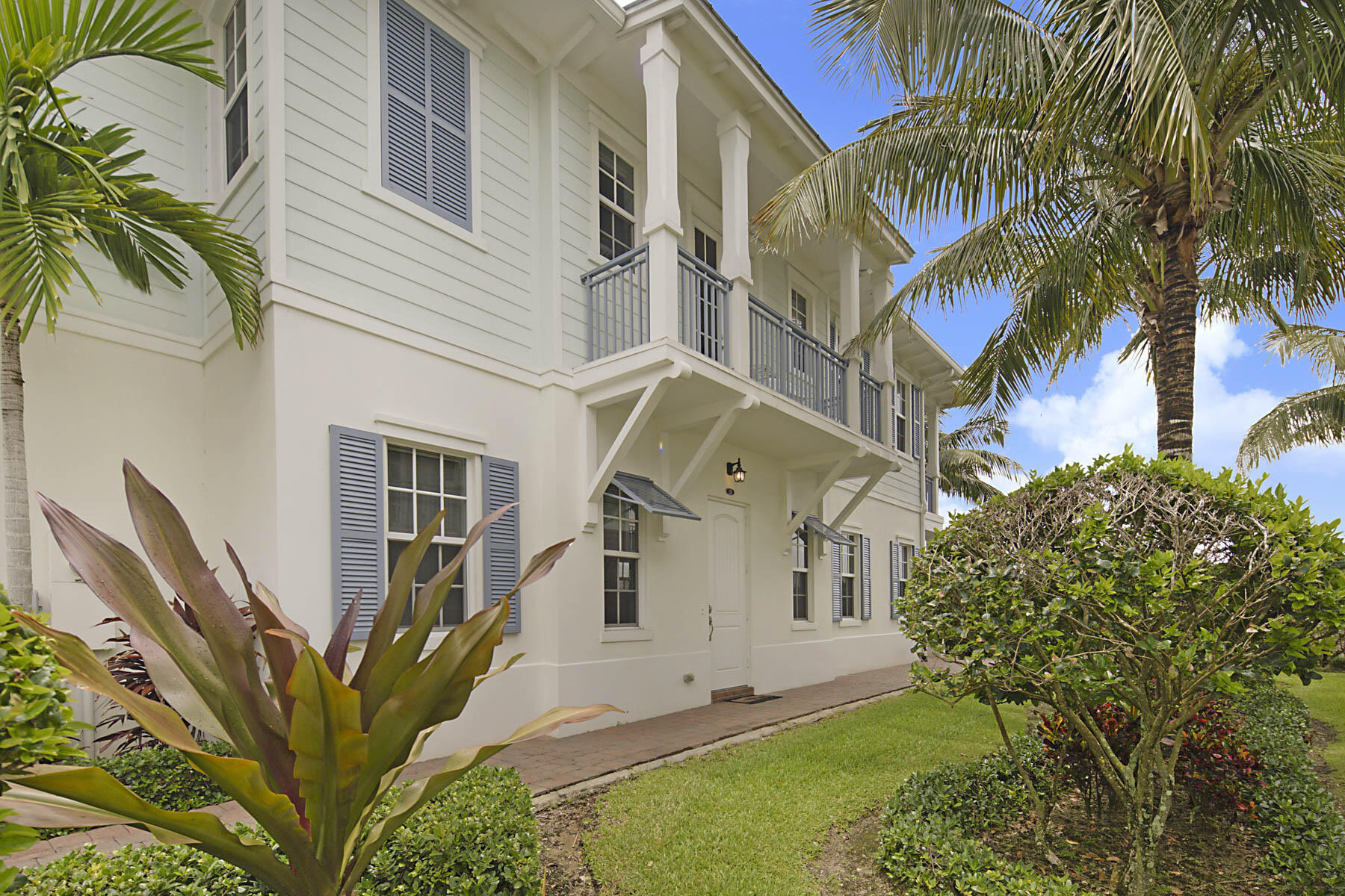 Two-story home with gray-shuttered windows, balconies, and tropical landscaping.