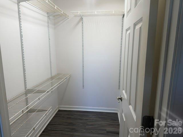 Walk-in closet with white wire shelving and dark wood-look flooring.