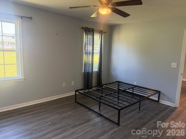 Empty bedroom with a black metal bed frame, gray flooring, and a ceiling fan with light.