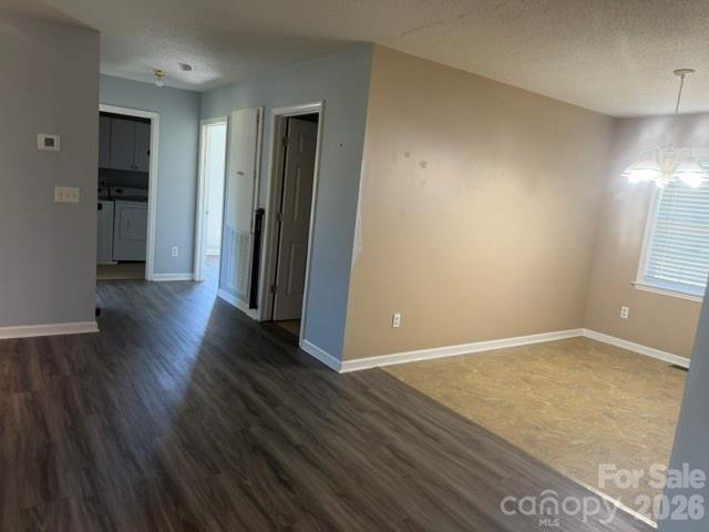 Vacant open-plan living and dining area with dark flooring, a chandelier, and the kitchen beyond.