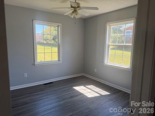 Empty bedroom with gray walls, two windows, dark flooring, and a ceiling fan.
