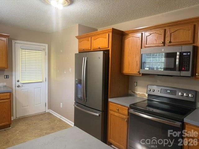 Kitchen with wood cabinets and stainless steel appliances; unfinished wall patches behind the range.