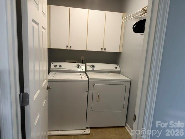 Laundry closet with washer and dryer beneath white cabinets and a wire shelf.
