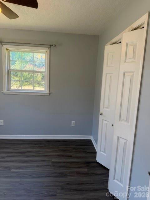 Vacant bedroom with dark wood-look flooring, a window, and open white closet doors.