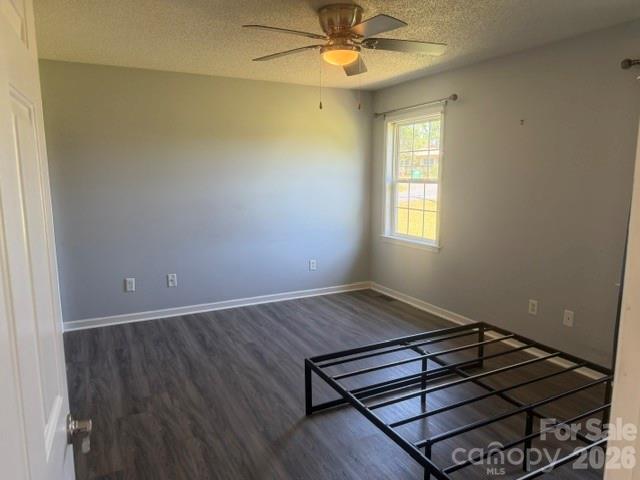 Empty bedroom with a black metal bed frame, dark flooring, and a ceiling fan.