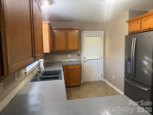 Kitchen with wood cabinetry, gray countertops, a double-basin sink, and a stainless steel refrigerator.