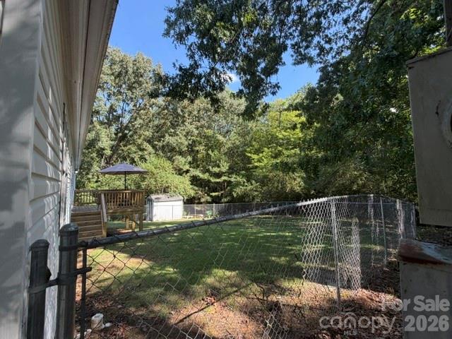Fenced backyard with a small deck, umbrella, lawn, and mature trees.