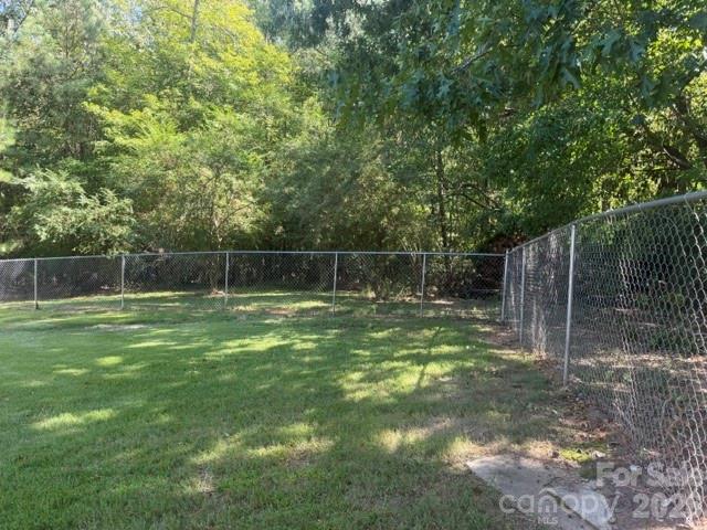 Grassy yard enclosed by chain-link fencing, with mature trees along the back.