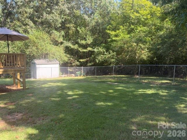 Backyard lawn bordered by a chain-link fence, with a shed and raised deck beneath mature trees.