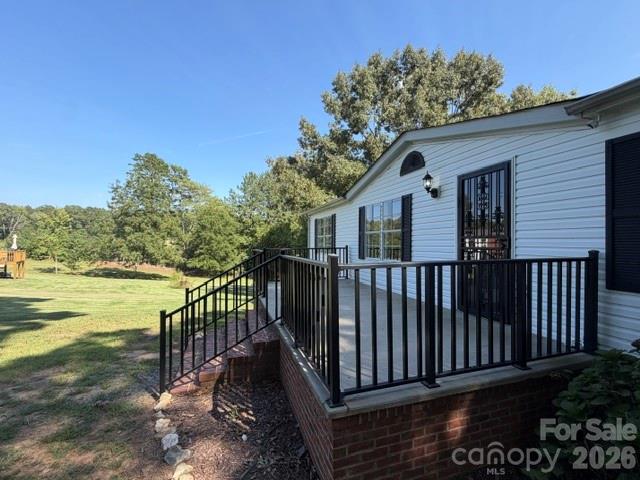 White-sided home with a raised black-railed deck and ramp overlooking a grassy, tree-lined yard.