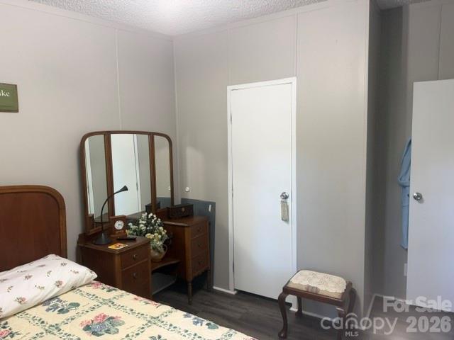 Bedroom with floral bedspread, wooden vanity, three-panel mirror, and dark flooring.