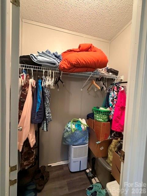 Walk-in closet with hanging clothes, a red comforter on the upper shelf, and storage bins below.