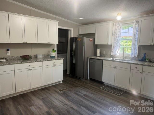 Kitchen with white cabinets, granite countertops, stainless steel appliances, and gray wood-look flooring.